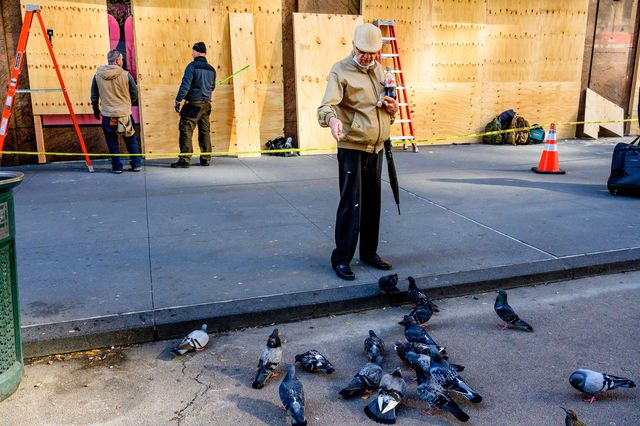 A man feeds a group of pigeons in front of a boarded up storefront in Midtown on Saturday.